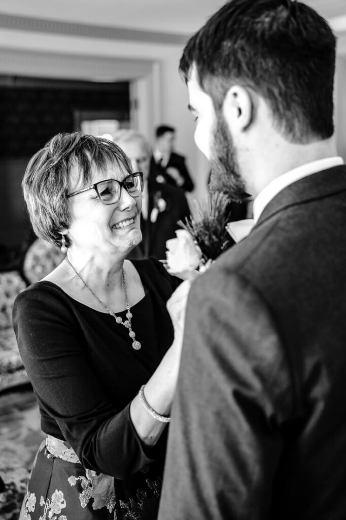 mom crying while pinning boutonniere on groom before his wedding at hotel saranac